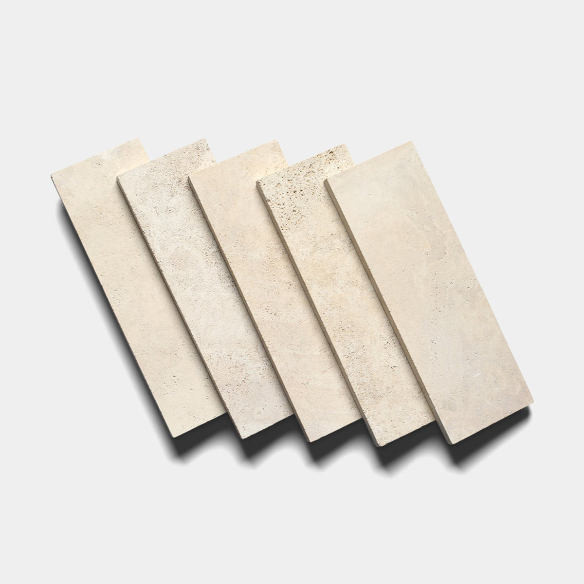 Five Zia Tile Mesa 4x12 rectangular beige Mexican Cantera stone tiles are arranged in a staggered row on a white background, each displaying subtle texture and shade variations and casting soft shadows below.