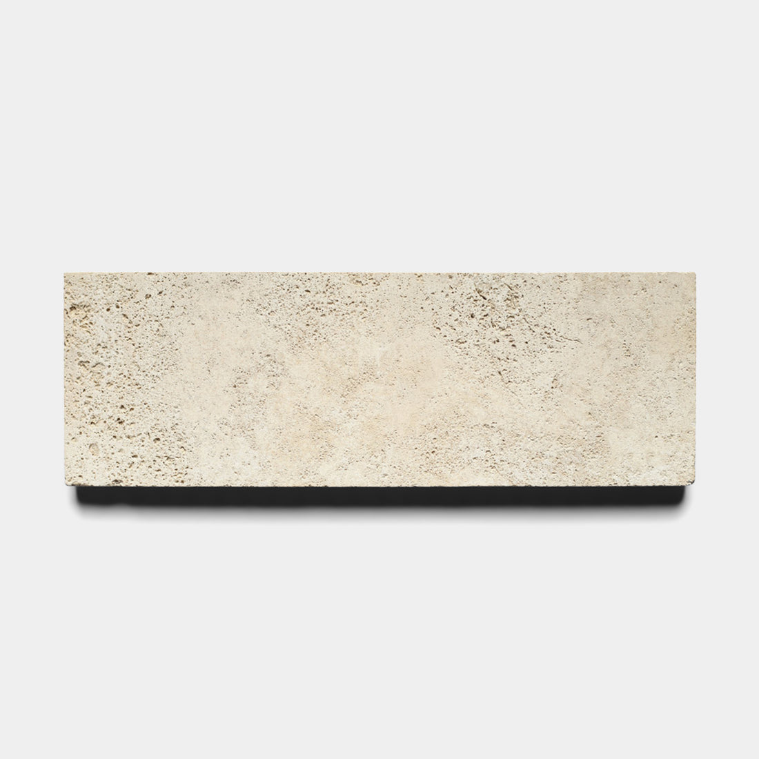The Mesa 4x12 tile by Zia Tile features a rectangular beige Cantera stone design with a rough, porous texture, set against a white background to highlight the natural beauty of this Mexican volcanic stone.