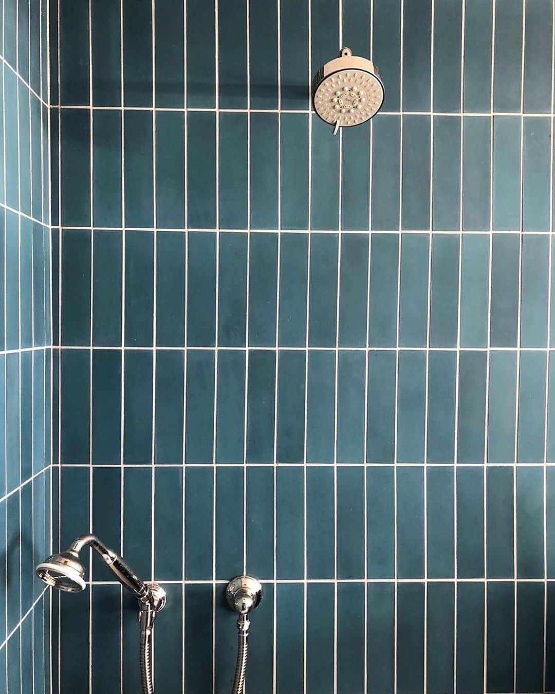 A shower featuring vertically arranged Midnight 2x8 tiles by vendor-unknown in teal blue, paired with chrome fixtures and a round overhead showerhead.