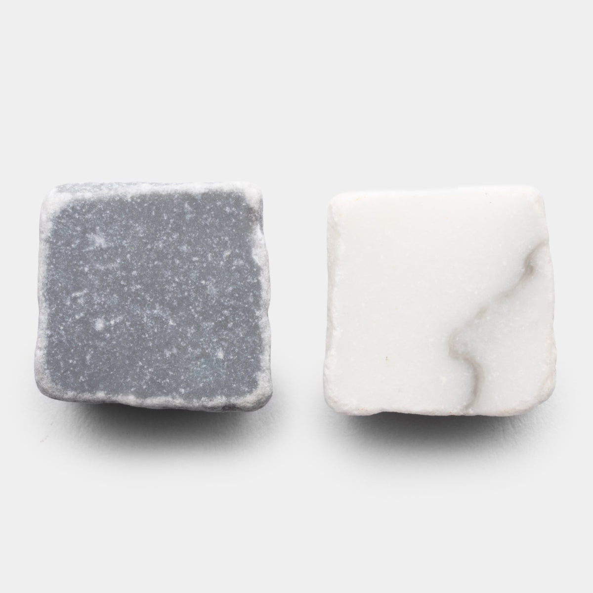 Two square stones from Zia Tile's Mini Check in Carrara + Bardiglio Imperiale: the left is gray with white speckles, the right is white with soft gray veining, both set on a light background.