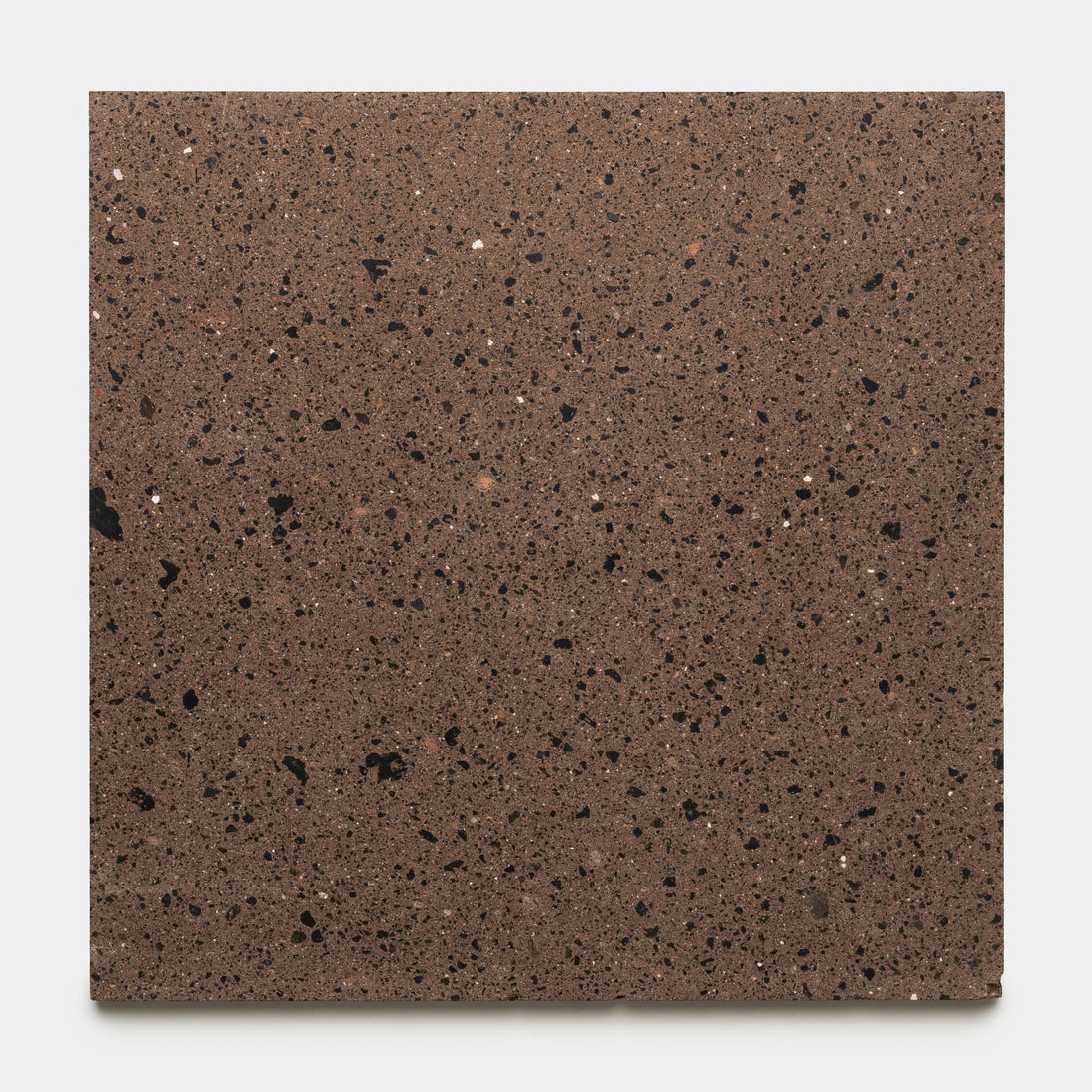 A 24x24-inch square sample of Zia Tile’s Moab, a brown granite tile featuring black, white, and reddish speckles reminiscent of a handmade design, is displayed on a plain white background.