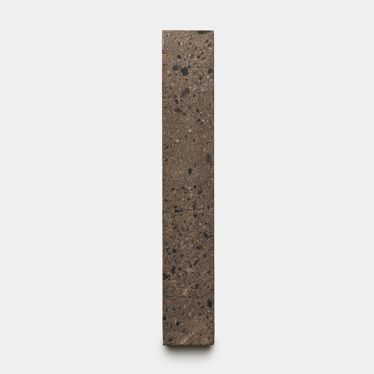 The Zia Tile Moab 2x12 features a tall, rectangular block of speckled brown and black stone, standing upright against a plain light gray background.