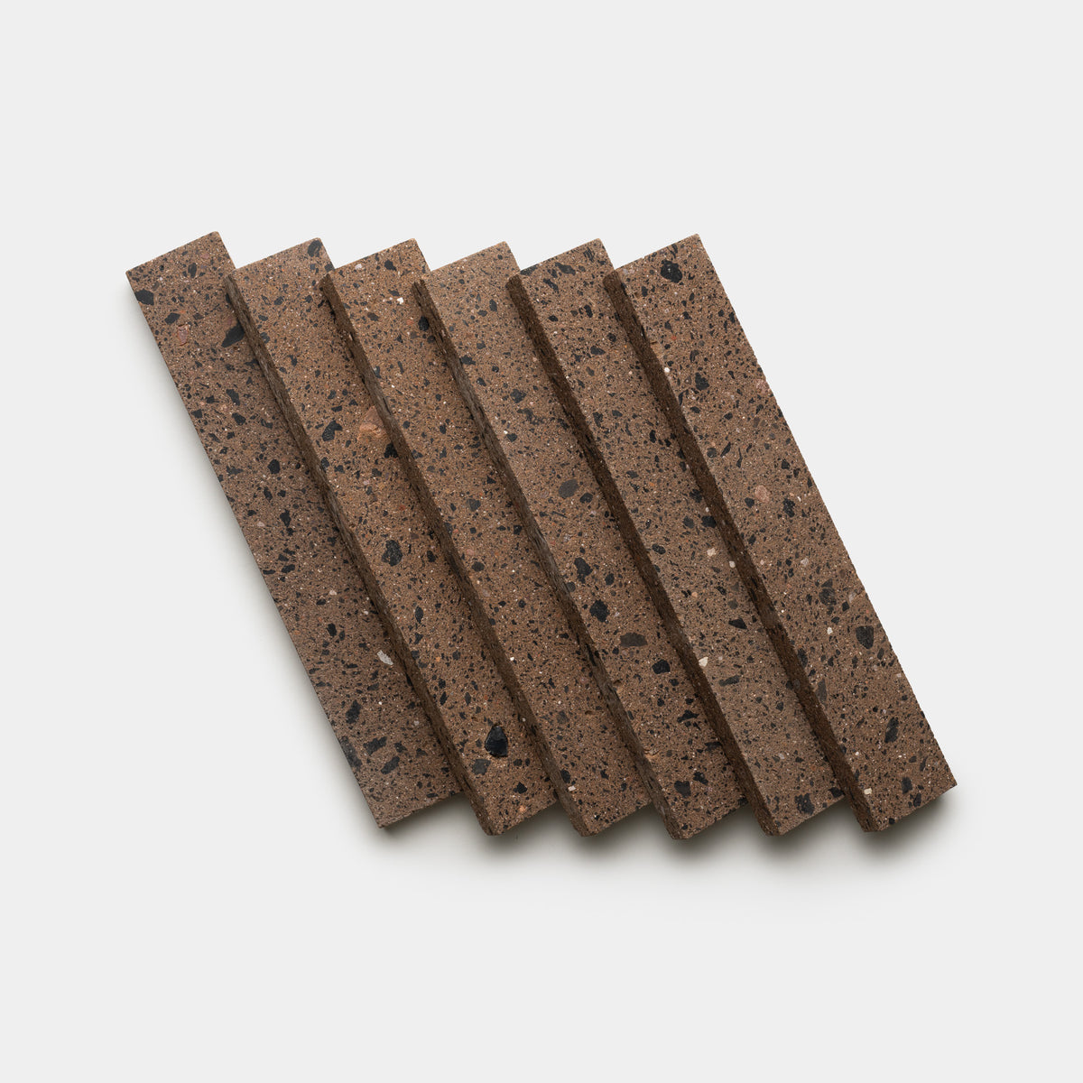 Six Moab 2x12 rectangular tiles by Zia Tile, in a brown hue with dark speckles and a porous texture, are arranged side by side on a white background.