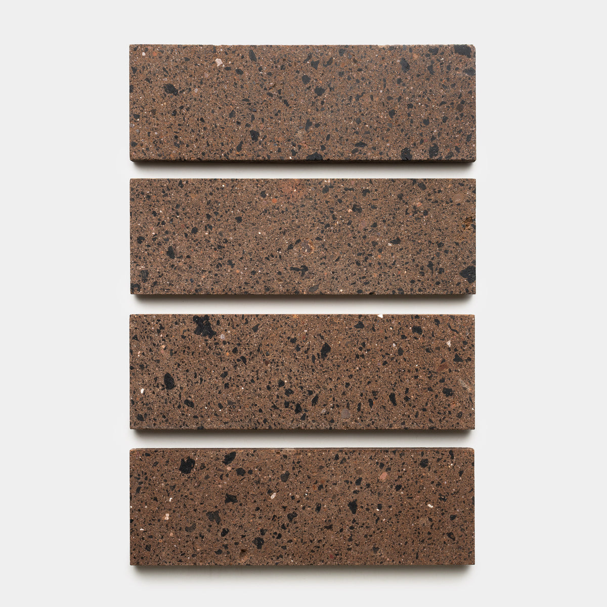 Four Zia Tile Moab 4x12 rectangular brown handmade tiles with black and tan speckles are evenly spaced in a vertical arrangement on a white background.