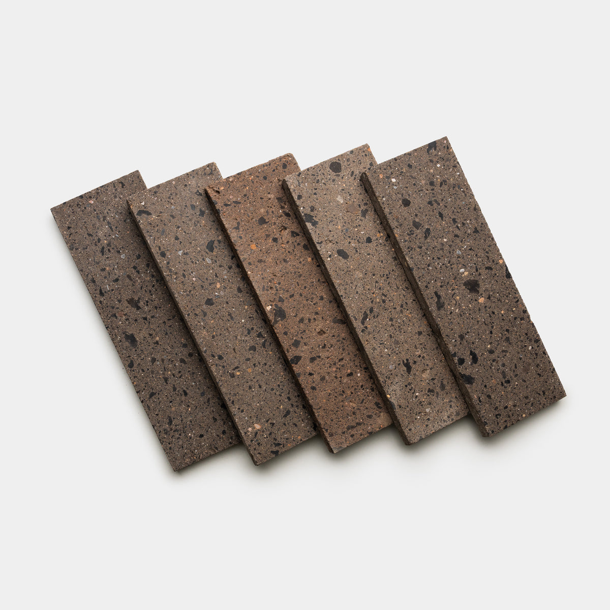 Five Moab 4x12 terrazzo samples by Zia Tile, in various brown and gray speckled finishes, are fanned out on a white background.