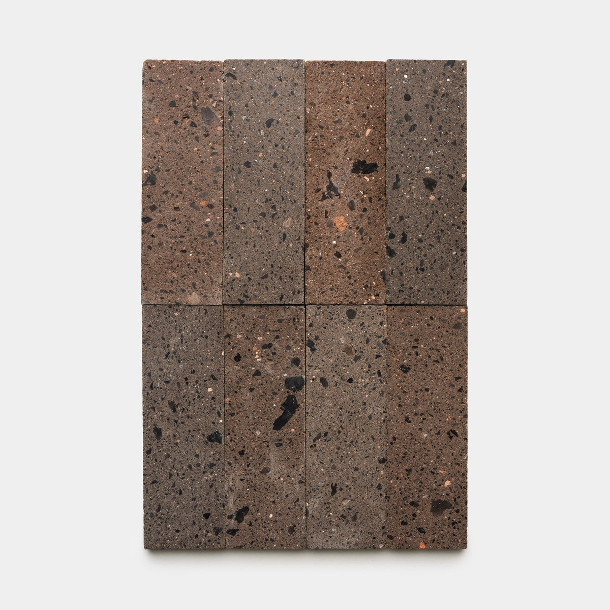 Eight Moab 4x12 rectangular volcanic stone bricks by Zia Tile are arranged in two columns and four rows on a white background, displaying brown and gray tones with natural porous textures and dark speckles.