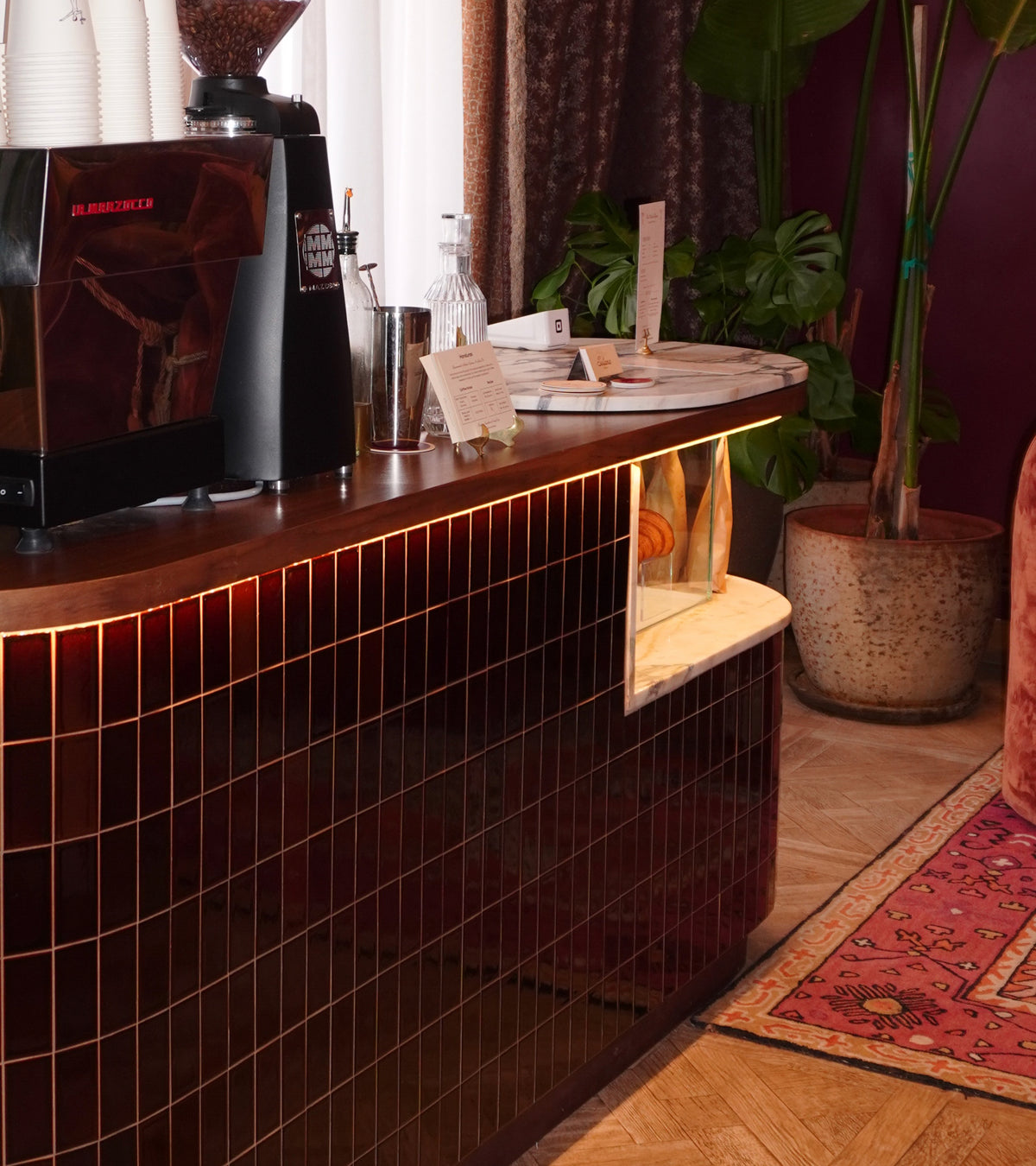A counter with a coffee machine on it, accented by stunning Zia Tile Molasses 2x4 tiles for a stylish and modern touch.