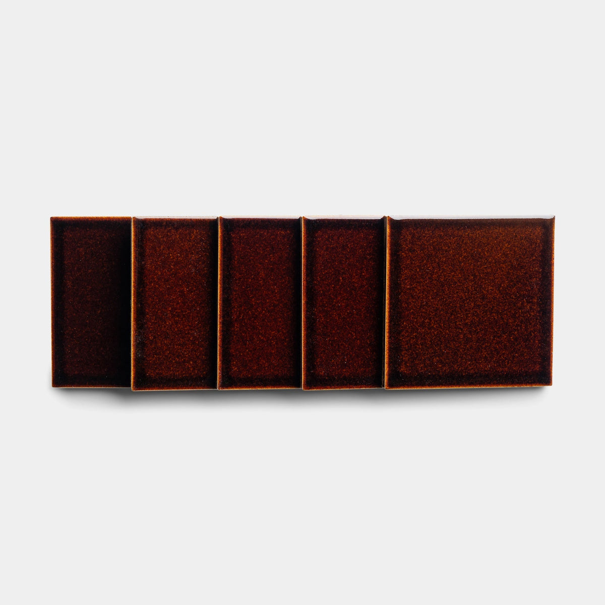Five Molasses 4x4 sample tiles from Zia Tile, varying in size, displayed side by side from smallest to largest. Each features a dark reddish-brown, speckled surface on a plain white background.