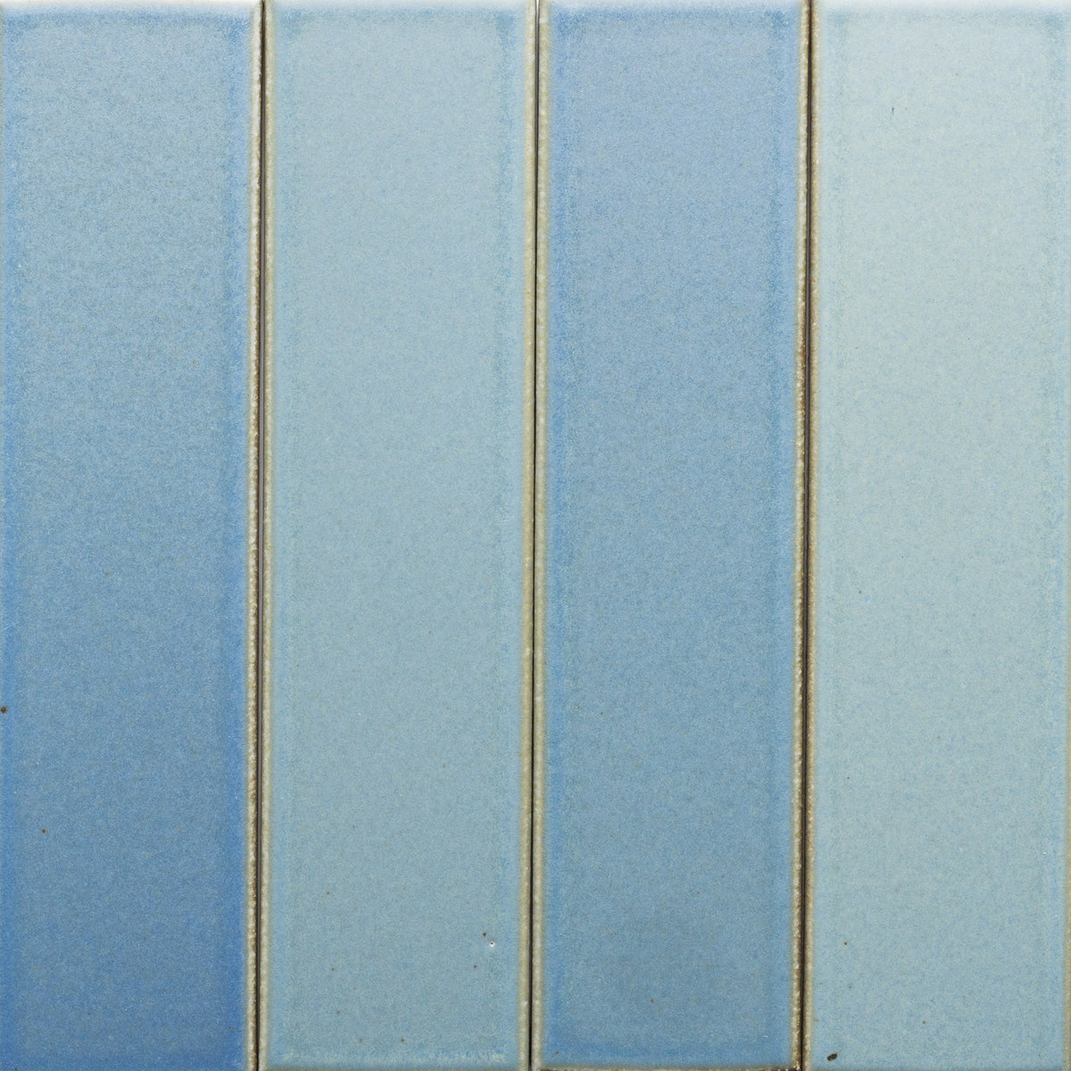 Four Morning Light + Flat ceramic tile samples by Zia Tile, each in a unique blue shade, are arranged side by side with thin beige grout lines. The tiles have a smooth, matte surface.