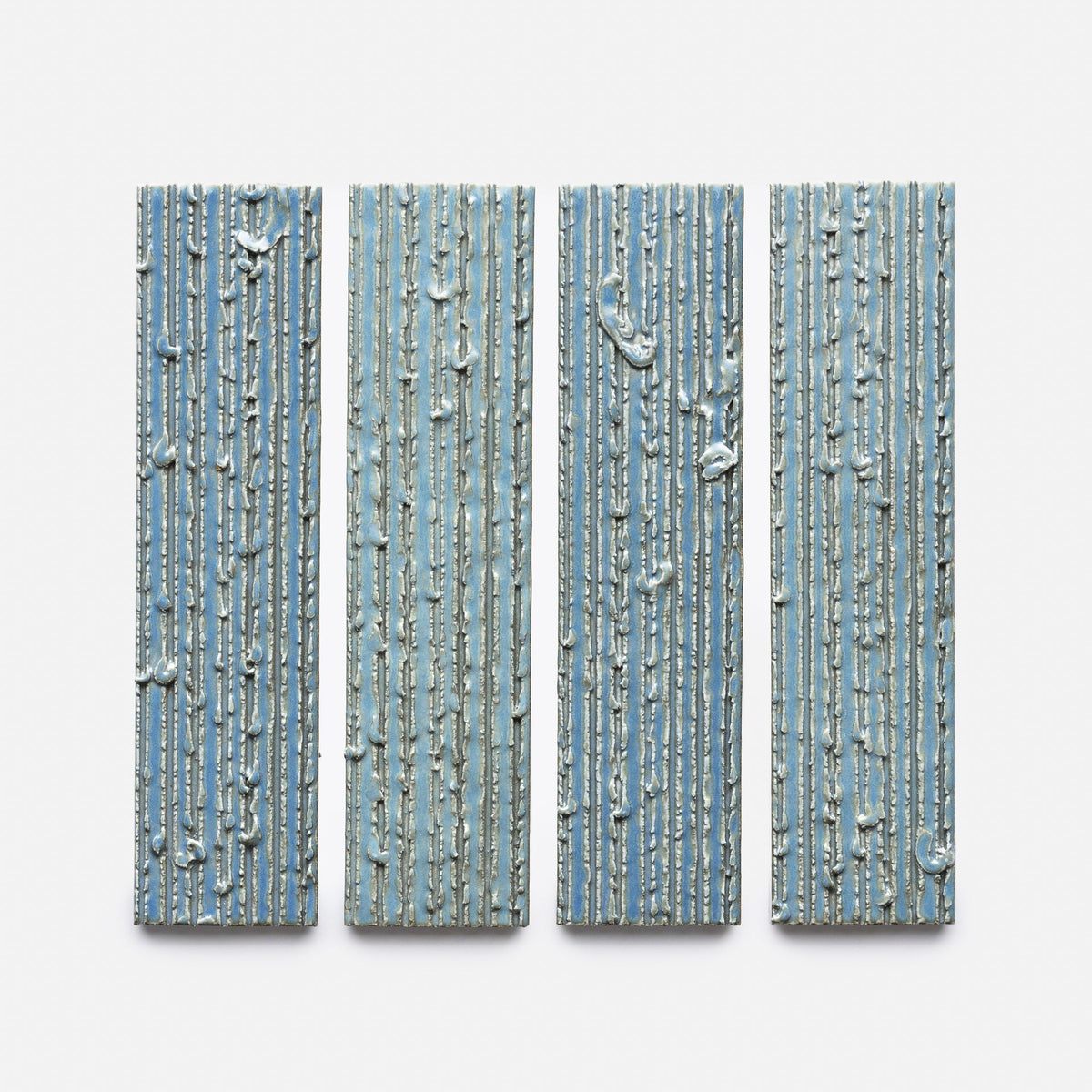 Four vertical rectangular panels from Zia Tile's Morning Light + Furrowed, Sample, feature textured blue surfaces with raised white lines, displayed side by side on a white background.