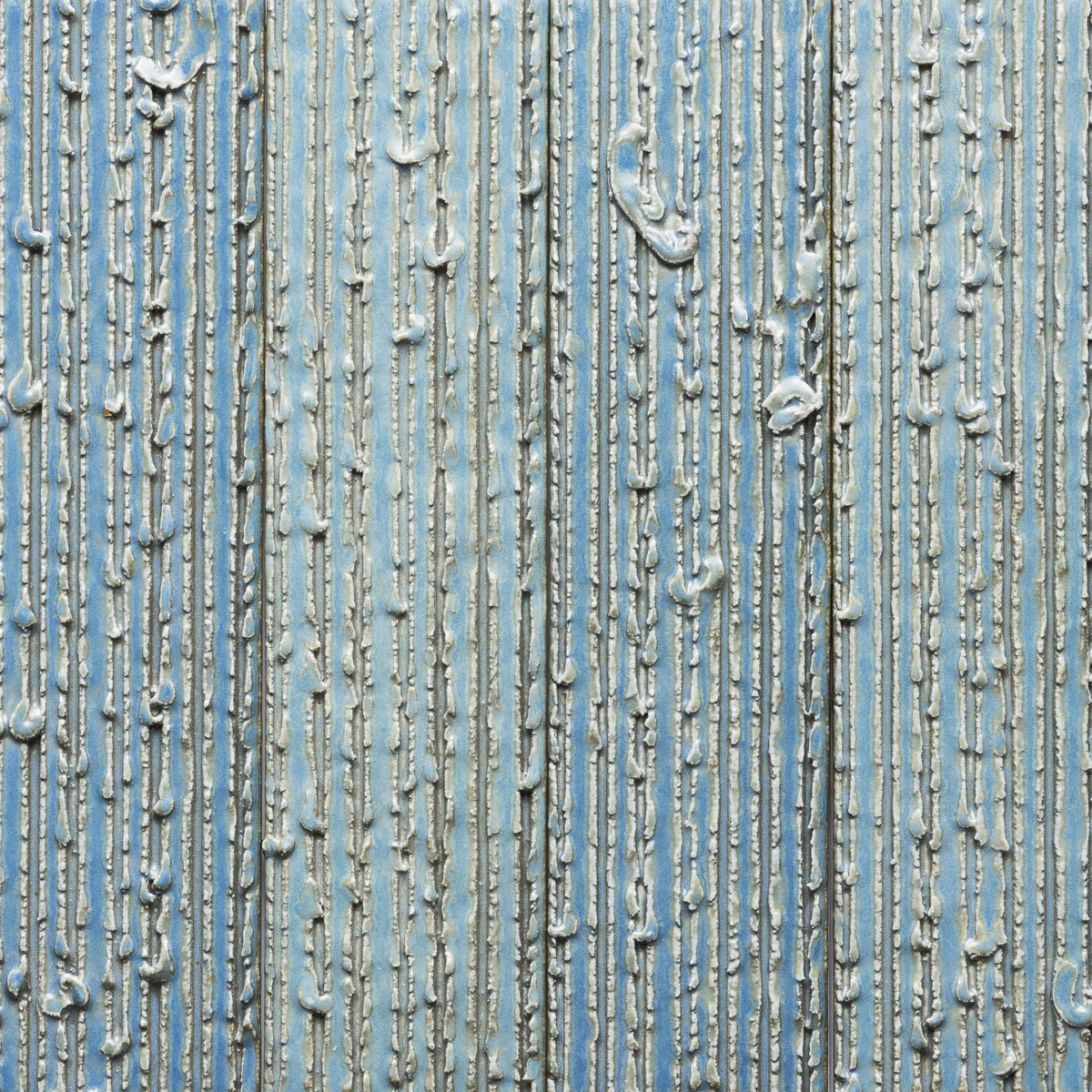 Morning Light + Furrowed Sample by Zia Tile features a textured blue surface with vertical and raised silver lines, adding uneven metallic patterns and dimension.