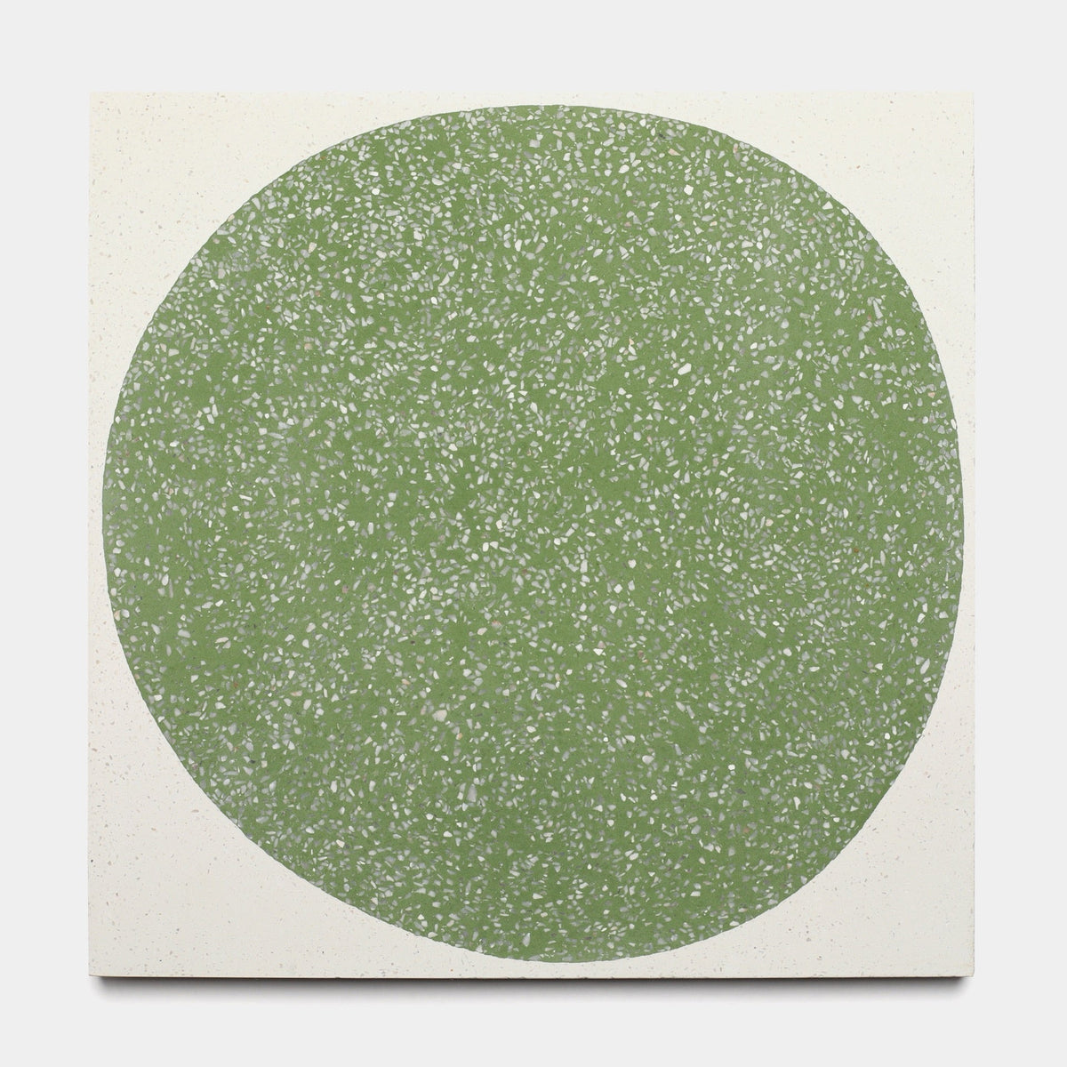 A large, green circle with white speckles fills most of an off-white square, creating an abstract, minimalistic design reminiscent of a tile sample. Product: Moxie Saguaro 12x12, Sample by Zia Tile.