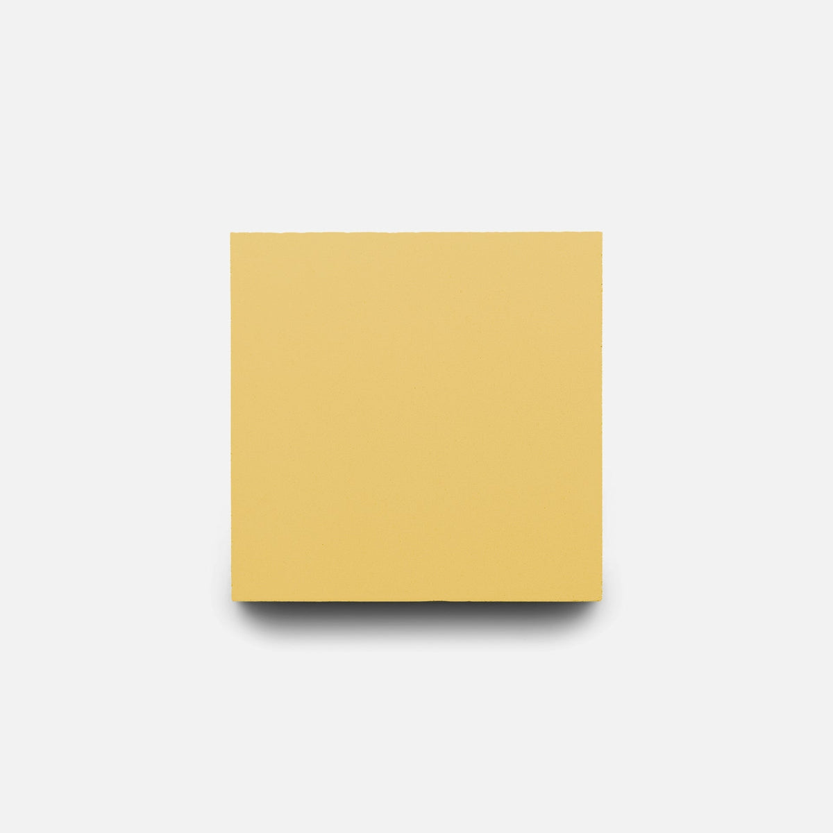 A single Mustard 4x4 tile sample by Zia Tile is centered on a white background, casting a soft shadow below—its minimalist style echoing the elegance of handmade craftsmanship.
