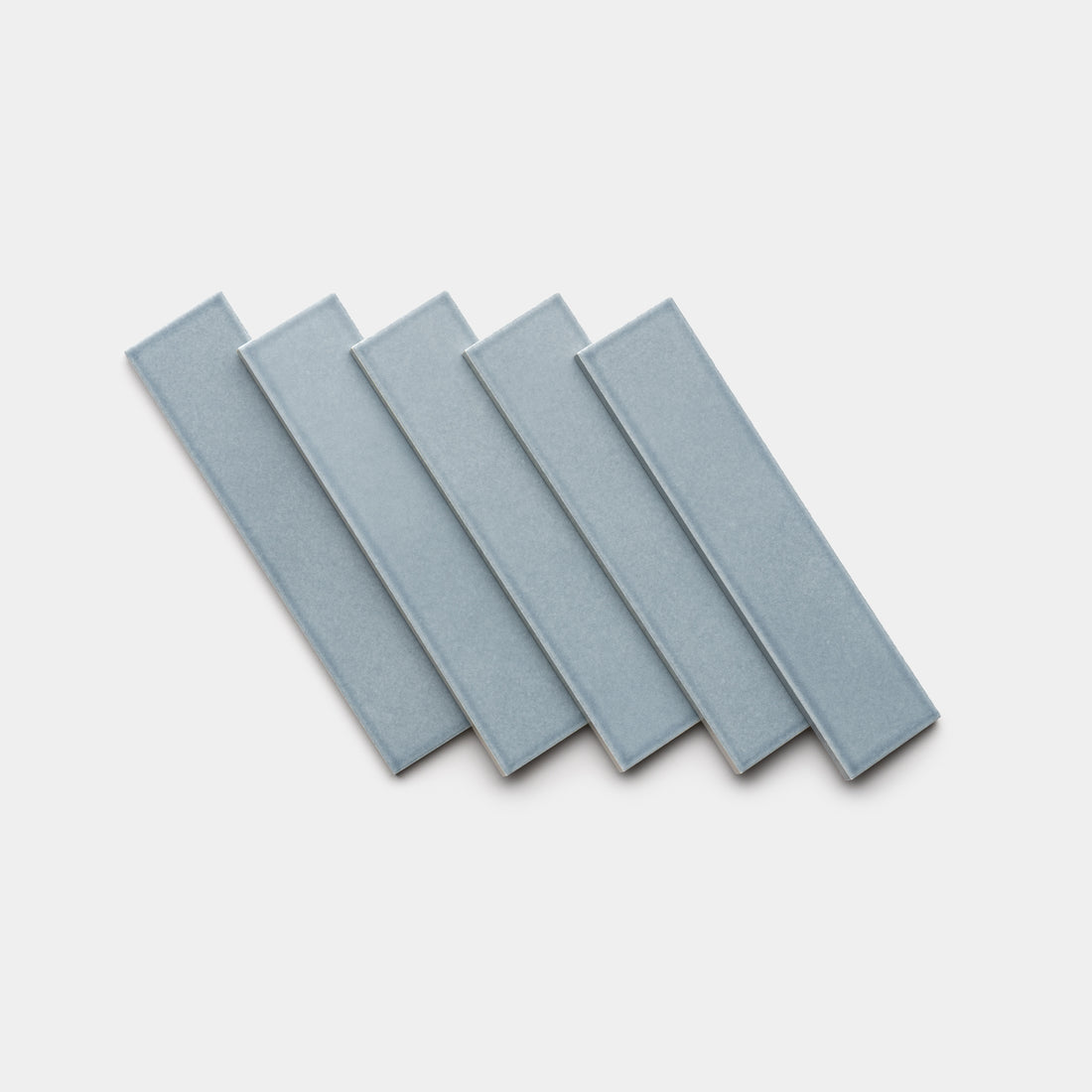 Five Mystic 2x8 rectangular ceramic tiles by Zia Tile, in light blue, are arranged in a slightly fanned-out, overlapping pattern on a white background.