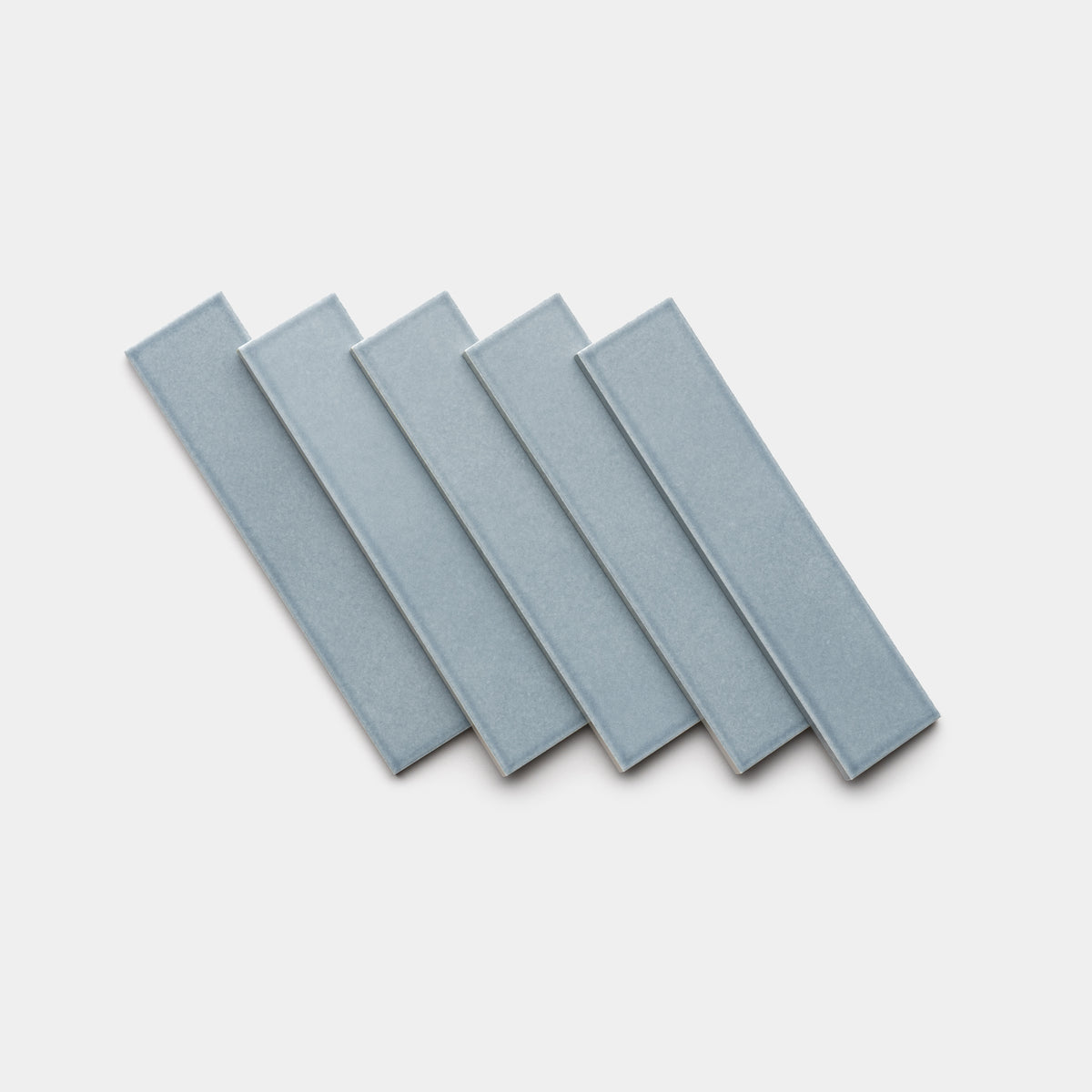 Five Mystic 2x8 rectangular ceramic tiles by Zia Tile, in light blue, are arranged in a slightly fanned-out, overlapping pattern on a white background.