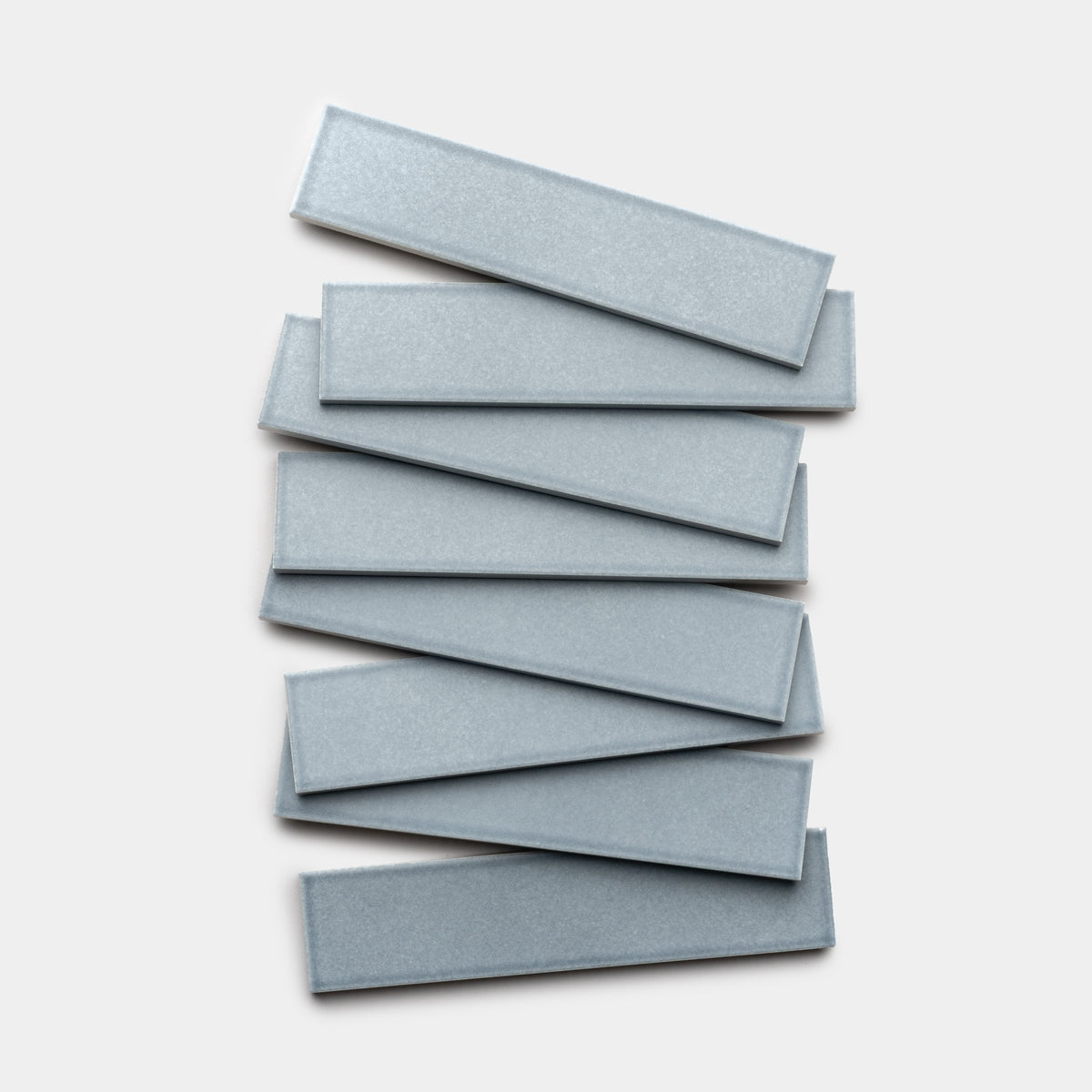 Seven Mystic 2x8 rectangular tiles by Zia Tile, in metallic gray, are arranged in a slightly overlapping, staggered stack on a white background.