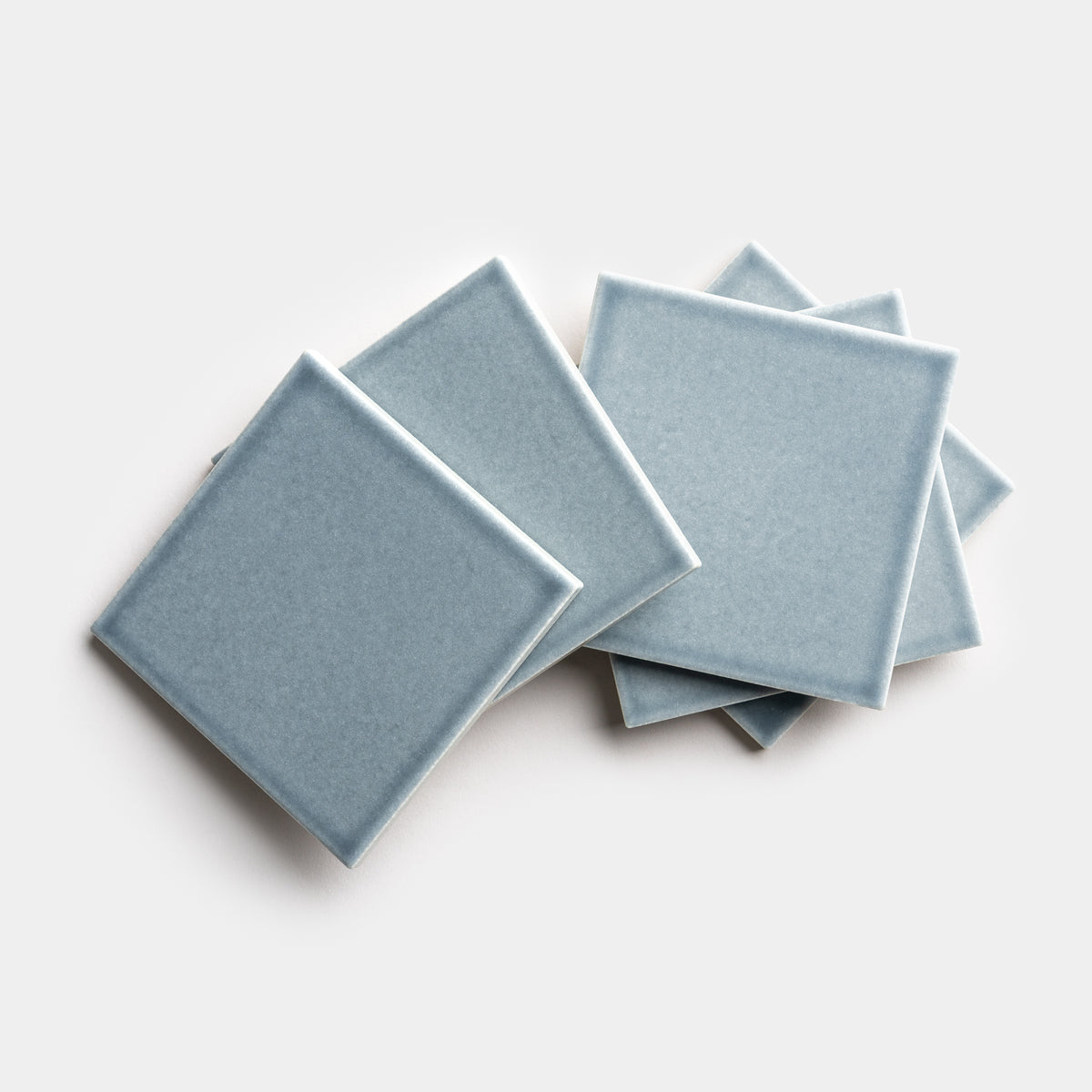 Five Mystic 4x4 tiles by Zia Tile, in a light blue square ceramic design, are arranged in an overlapping pattern on a white background.