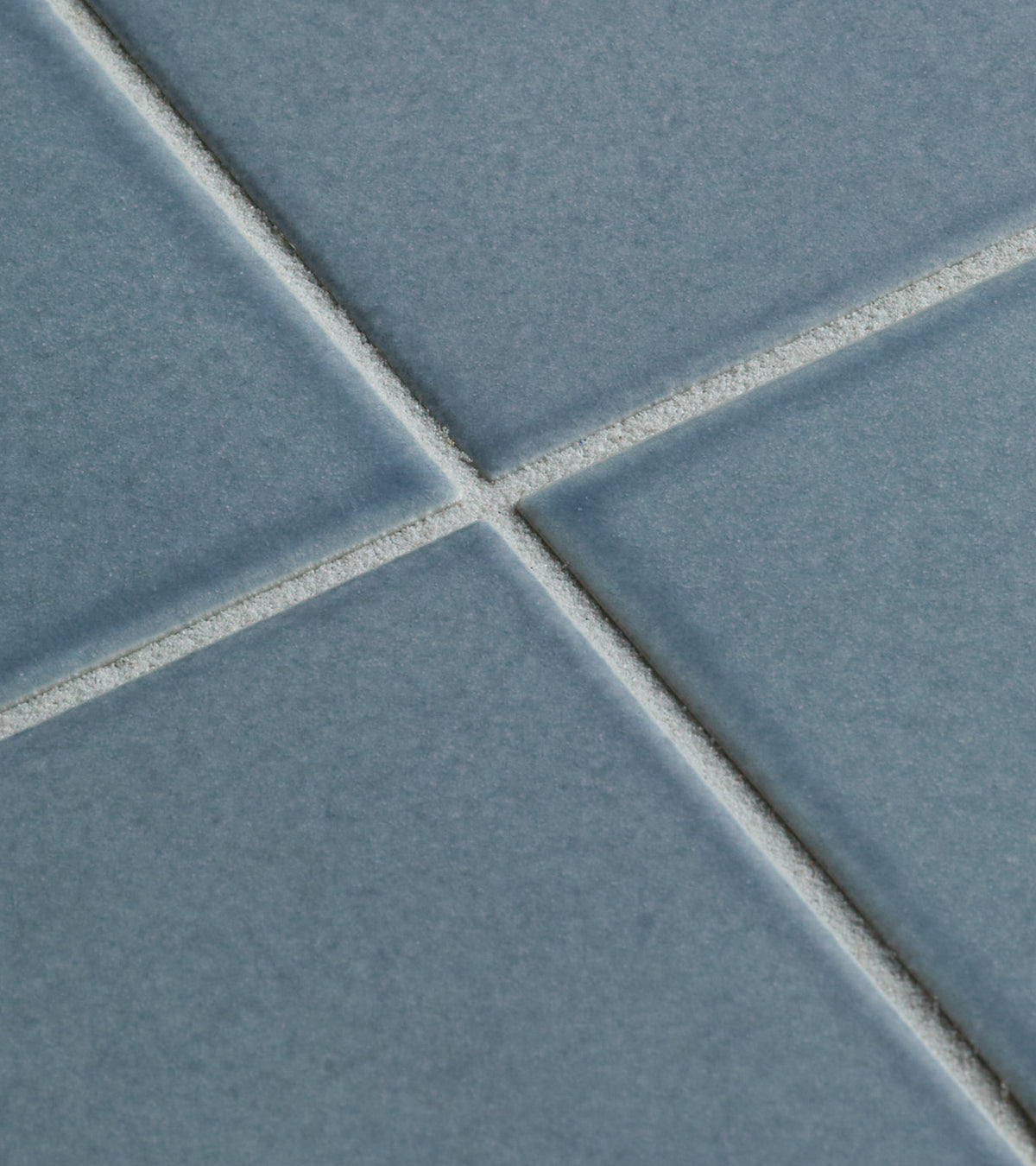 Close-up of four Mystic 4x4 tiles by Zia Tile in a grid pattern with white grout lines at the center. The blue ceramic tiles feature a matte texture and smooth surface.