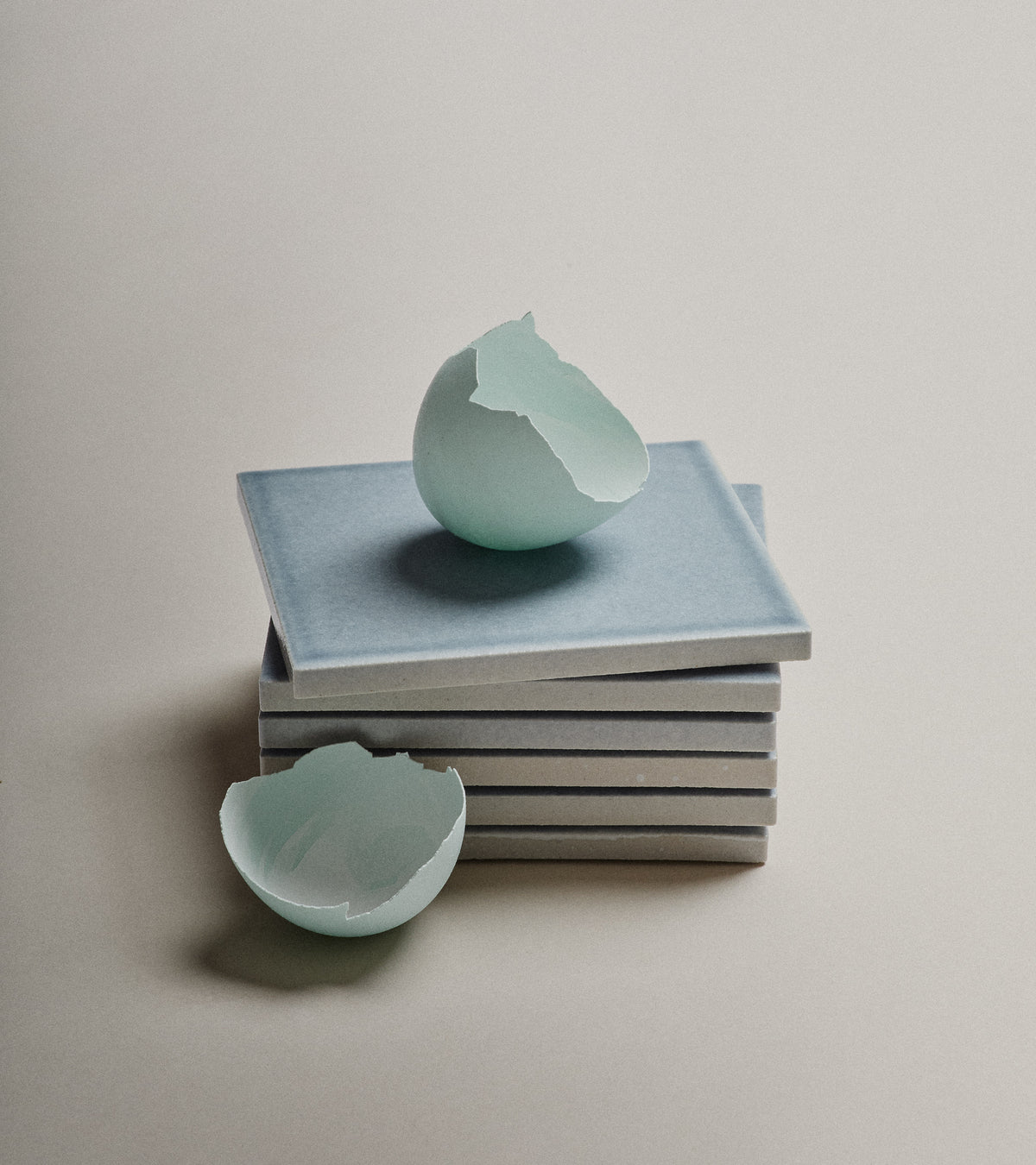 A light blue eggshell, broken in half, rests on a stack of Mystic 4x4 tiles by Zia Tile, set against a neutral background.