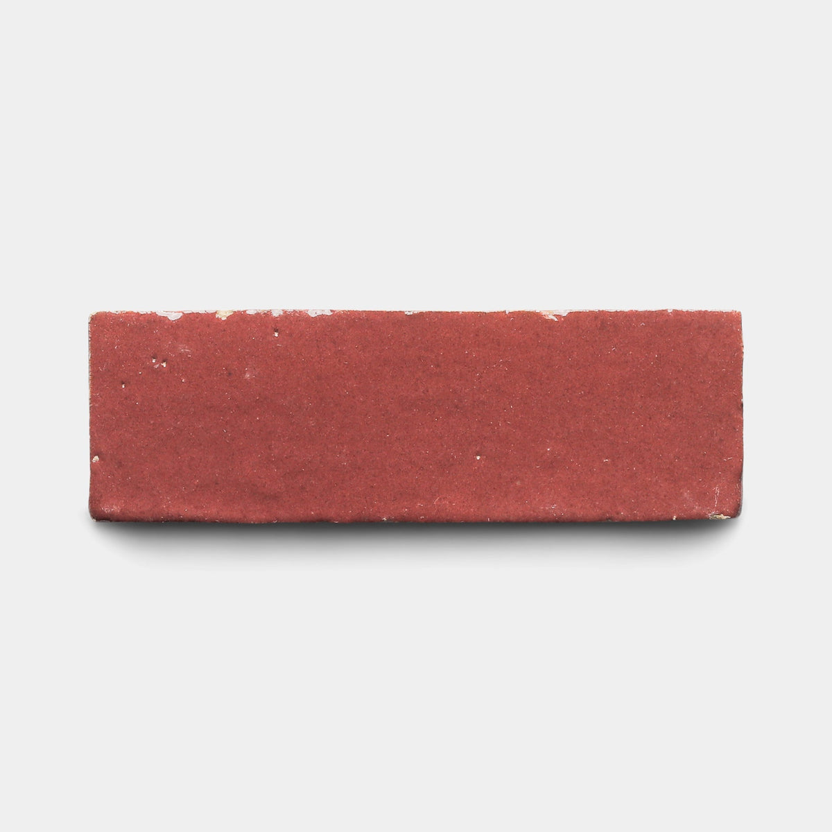 A sample of Zia Tile’s Nana’s Lipstick 2x6, a red cement tile with a smooth top surface, viewed from above against a plain white background.