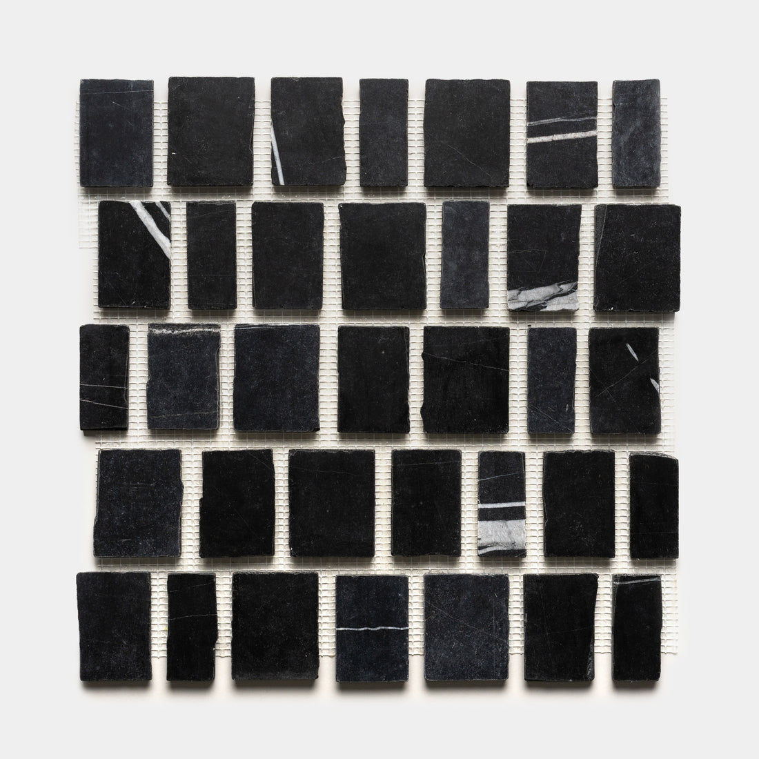 Scarpa in Nero Marquina by Zia Tile features a 5x5 sheet of black marble tiles, each with unique white veining, mounted on a white mesh backing.