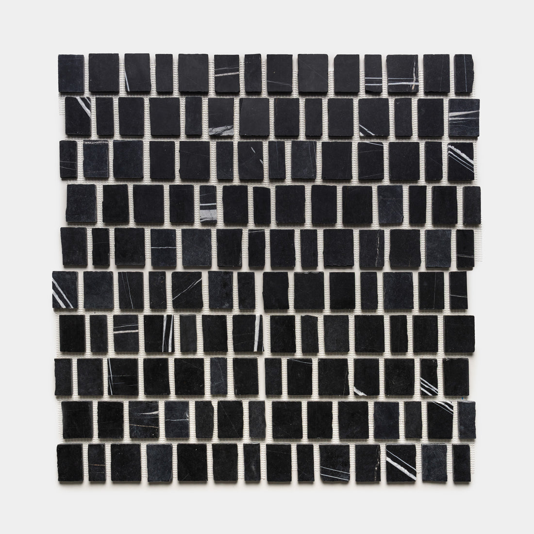 Scarpa in Nero Marquina by Zia Tile features small, black rectangular tiles with occasional thin white streaks, arranged in a neat square grid on a white background.