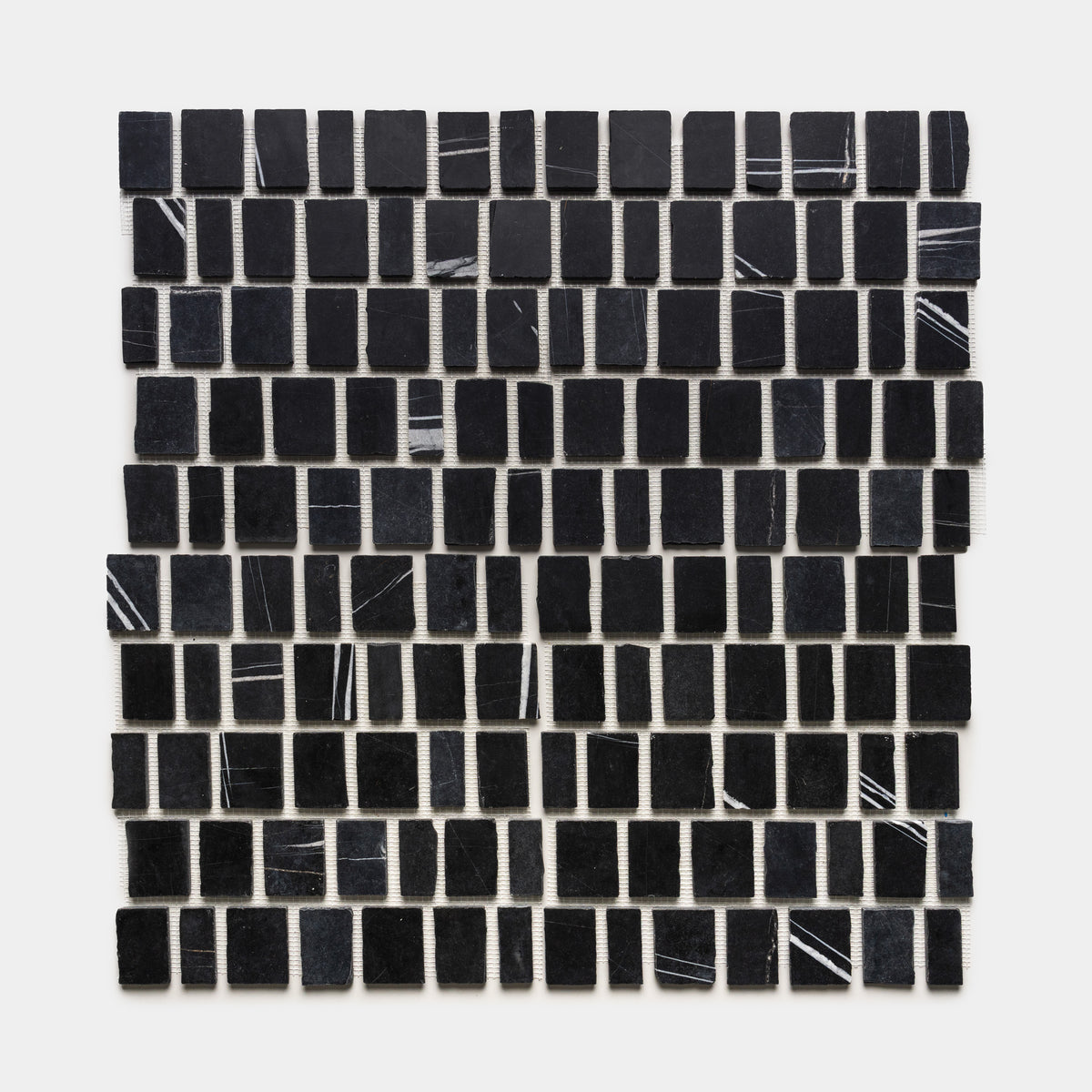 Scarpa in Nero Marquina by Zia Tile features small, black rectangular tiles with occasional thin white streaks, arranged in a neat square grid on a white background.