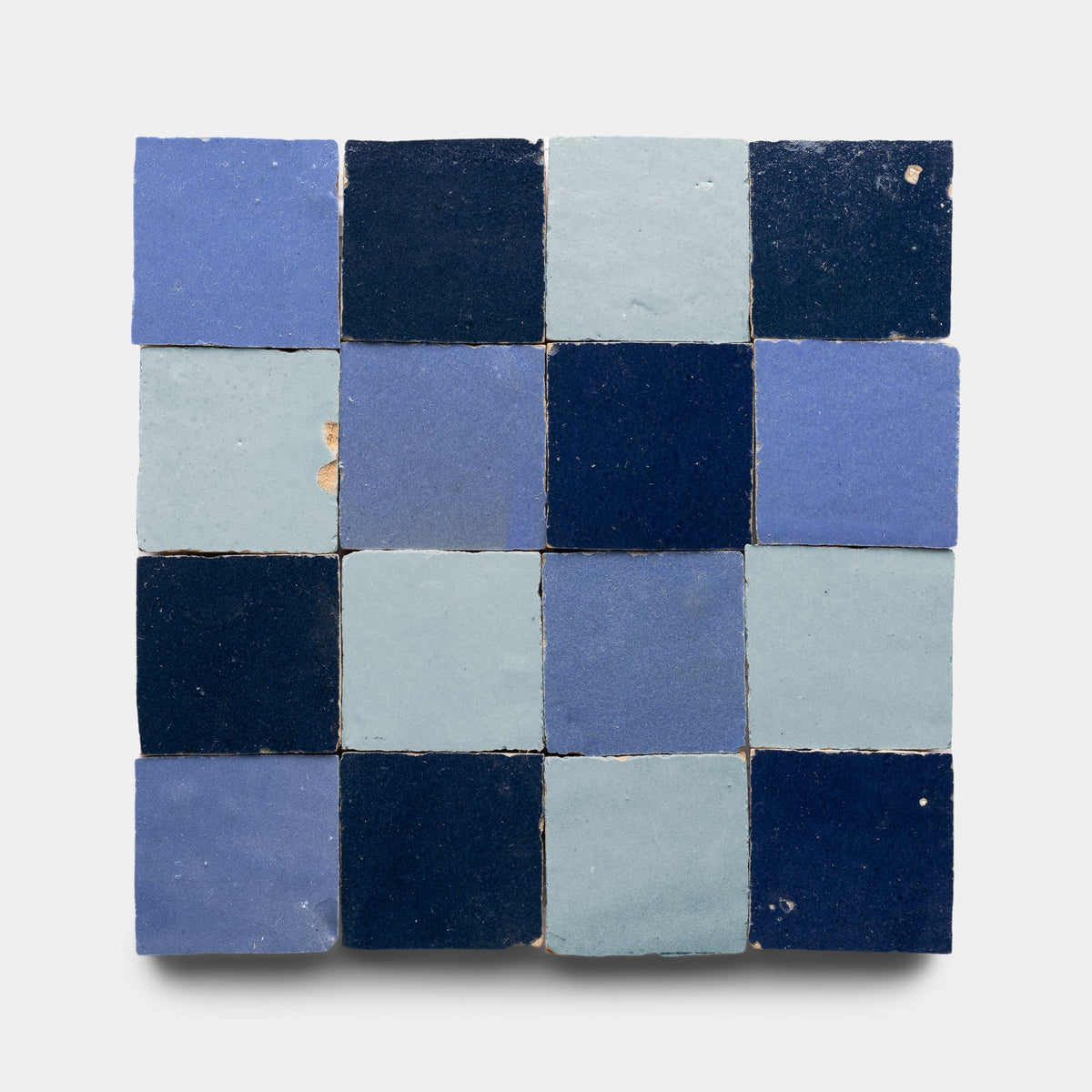 The Zia Tile Night Blue + Skylight + Portuguese Blue Checkerboard Sample features 16 handmade tiles in a 4x4 grid with matte finish and slightly uneven edges, showcasing alternating blue shades for a unique, artisanal look.