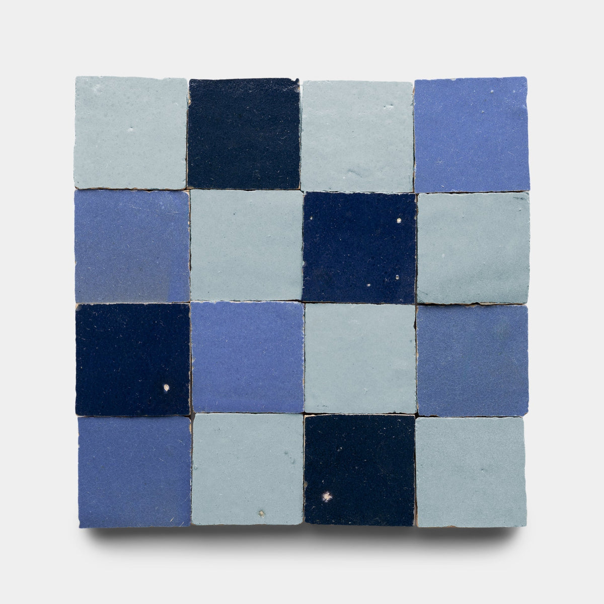 The Zia Tile “Night Blue + Skylight + Portuguese Blue Checkerboard, Sample” features sixteen handmade tiles in four rows and four columns, displaying blue shades from light to navy—ideal for bringing a touch of artistry to any space.