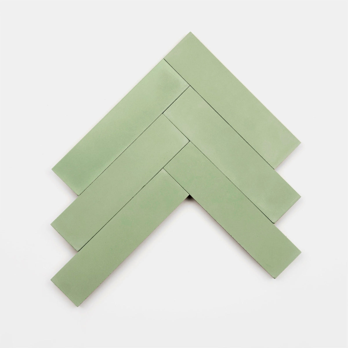 Five rectangular, light green Dune 2x8 sample tiles by Zia Tile are arranged in a herringbone pattern on a plain white background, creating an elegant tile display.