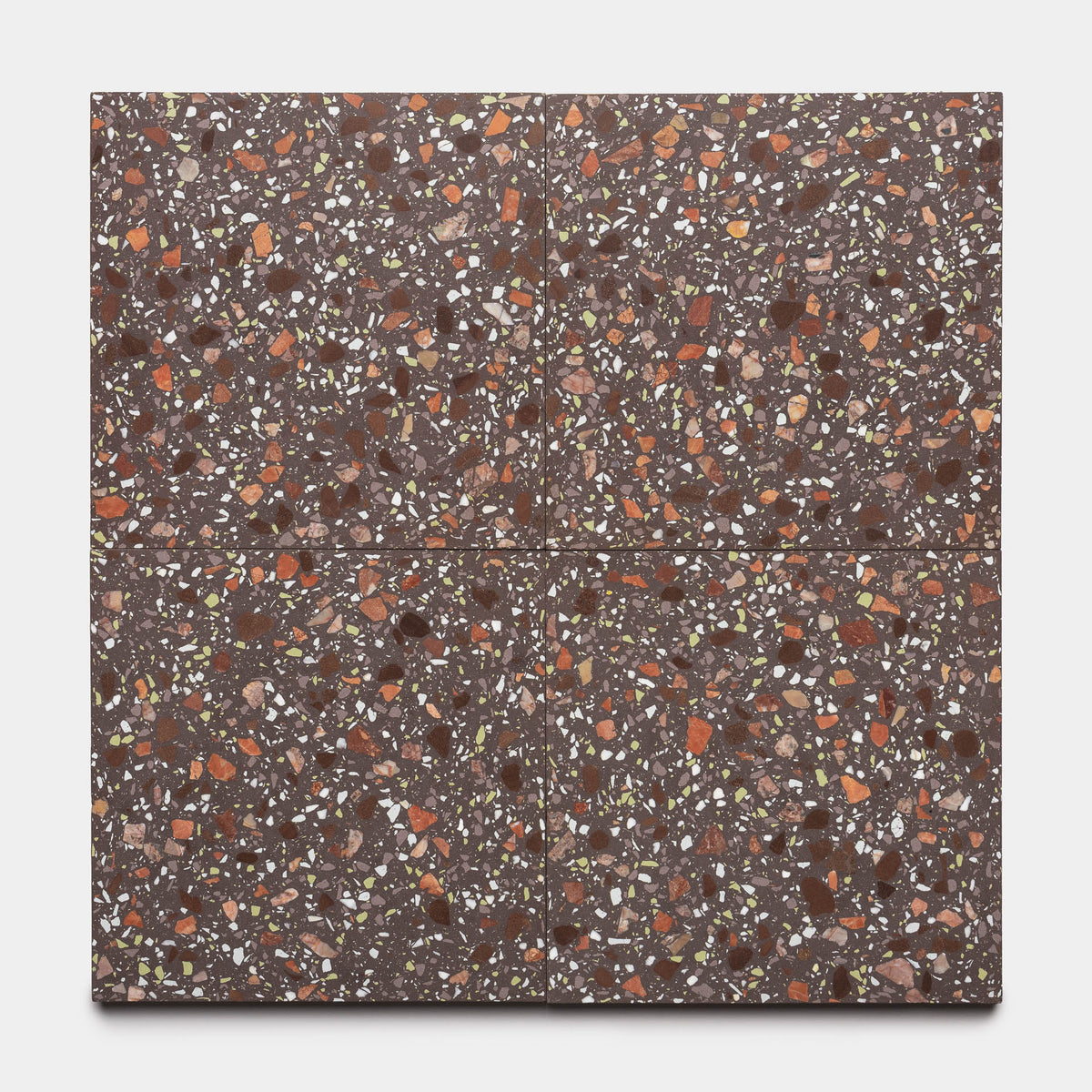 Zia Tile’s Nocino 12x12 features four square terrazzo tiles with a dark brown base, showcasing stone chips in orange, red, white, and beige for a seamless look.