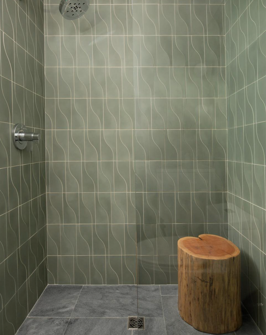 The Nouveau Zeppelin by vendor-unknown features green wavy-patterned tiles, gray cement tile flooring, a modern showerhead, and a wooden stump stool in the corner for a minimalist shower design.