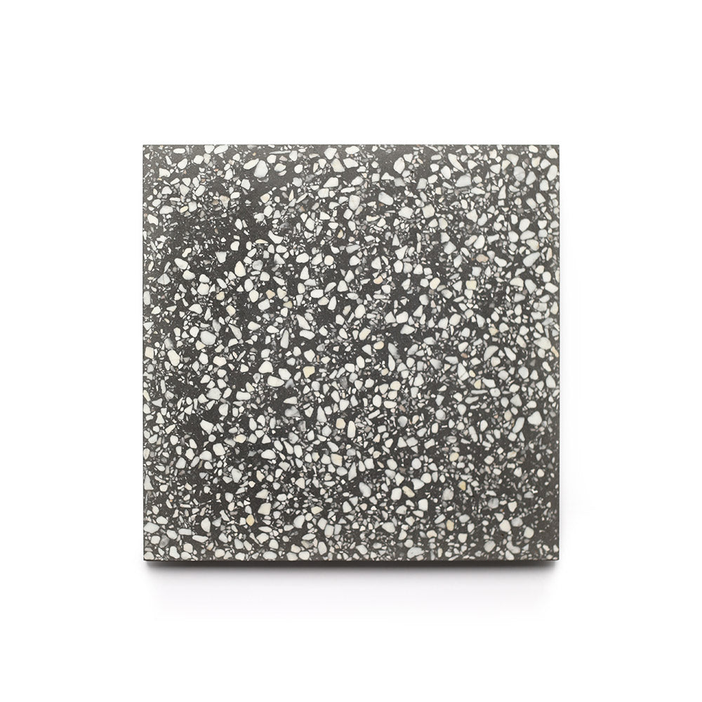 Oscar 6x6 by Zia Tile is a square terrazzo tile sample featuring a dark grey background with irregular white and light grey stone chips, shown against a plain white backdrop.