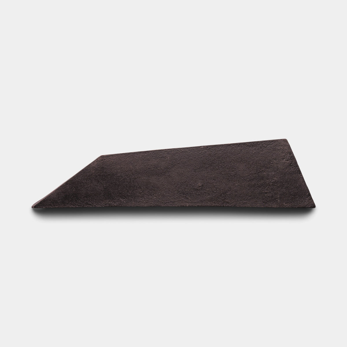 A single, flat, dark brown, irregularly shaped wedge of Tornillo + Oscura, Sample by Zia Tile is placed on a white background.