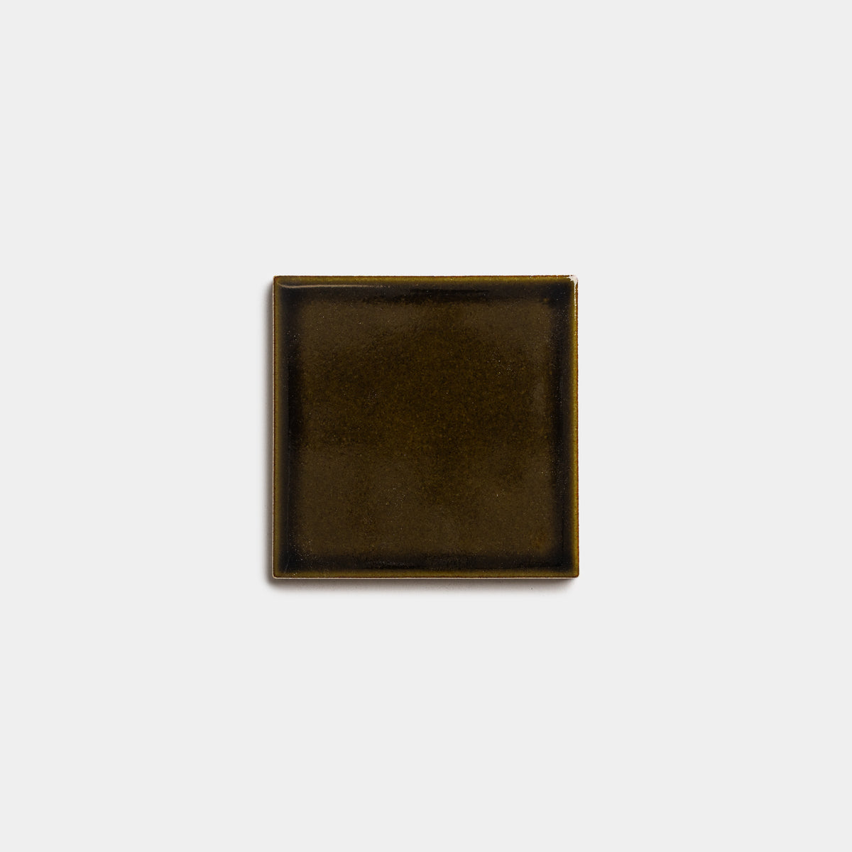 The Oud 4x4 by Zia Tile is a small, square, dark brown ceramic plate with slightly raised edges, shown against a plain white background.