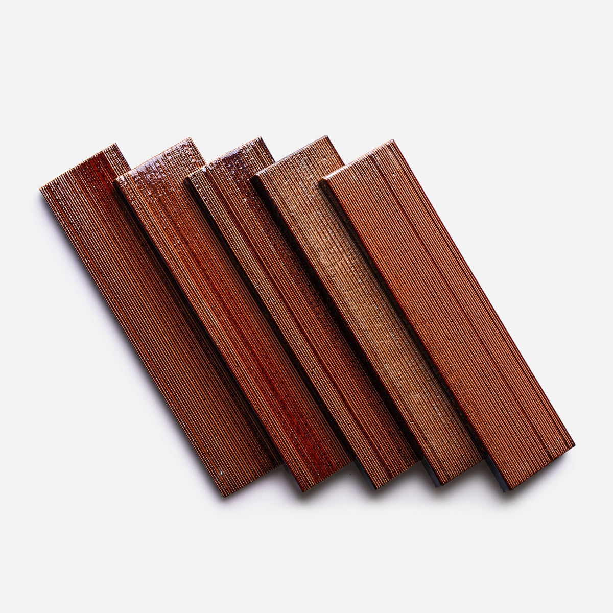Five rectangular, oxblood-colored tiles with an etched texture from Zia Tile's Oxblood + Etched sample are arranged in a fanned-out pattern on a white background.