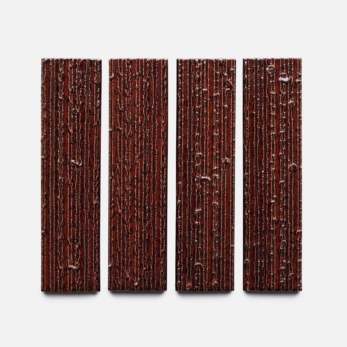 Four Oxblood + Furrowed, Sample chocolate bars by Zia Tile, each rectangular with textured vertical grooves, are evenly spaced in a row on a white background.