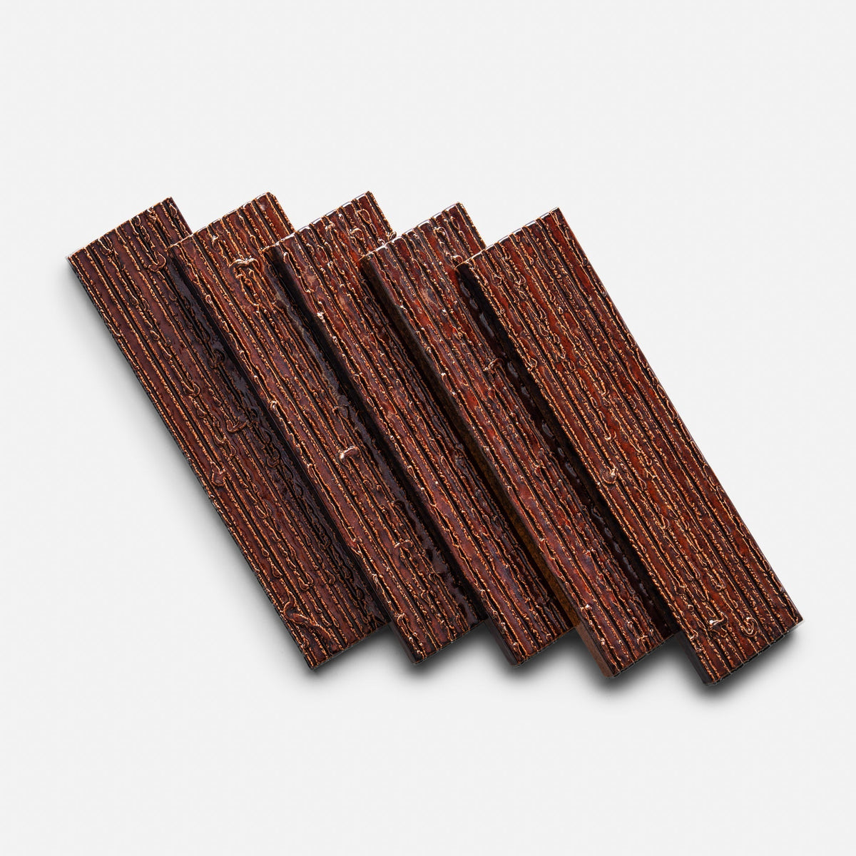 Five Oxblood + Furrowed, Sample tiles from Zia Tile are arranged diagonally on a plain white background, each tile slightly overlapping the next. The tiles feature a ridged texture and visible layered design.