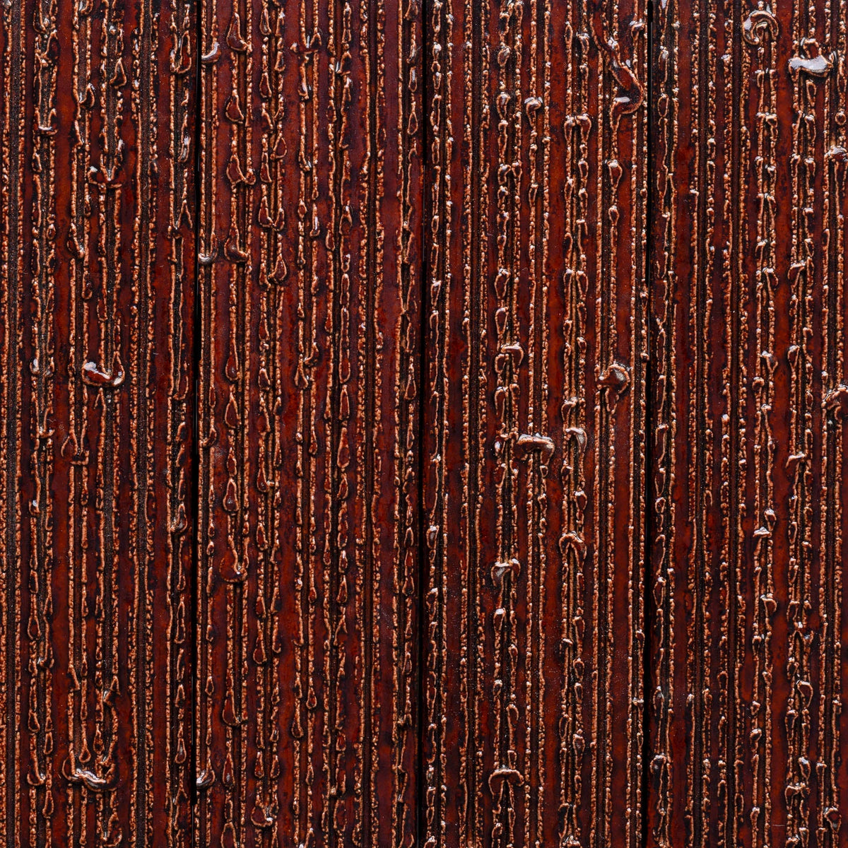 Close-up of Oxblood + Furrowed, Sample by Zia Tile showing a glossy, textured dark brown surface with vertical ridges and uneven lines that resemble melted material on wood or metal.