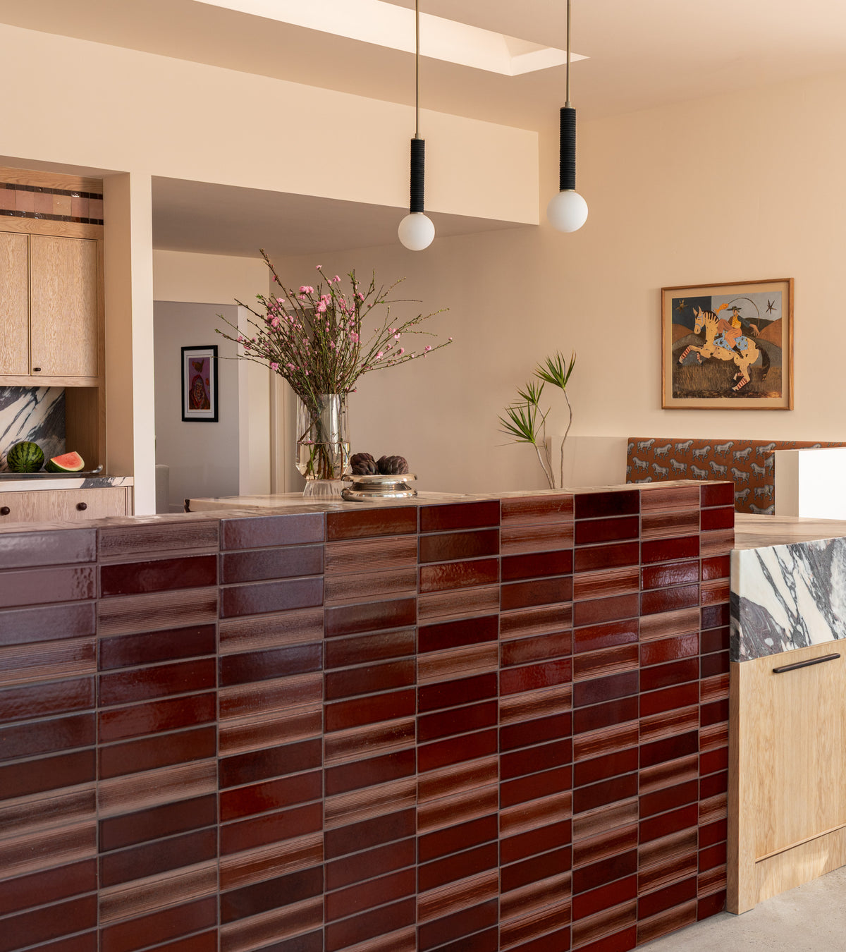 A kitchen island faced with Oxblood + Etched glossy, dark red rectangular tiles, featuring a marble countertop and wooden cabinets.
