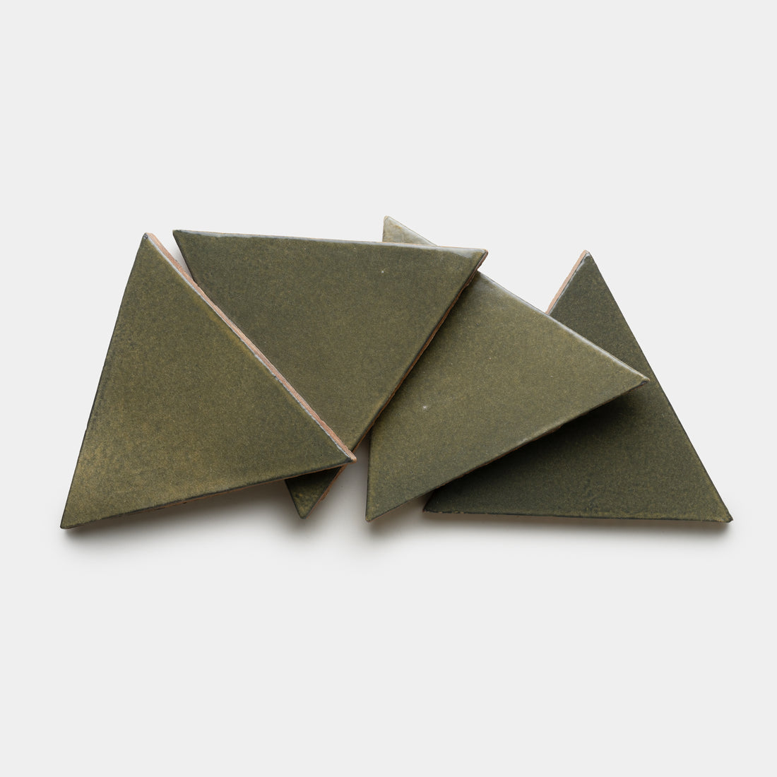 Five Oyamel Triangle tiles by Zia Tile in olive-green ceramic are arranged in a slightly overlapping, irregular pattern on a white background.