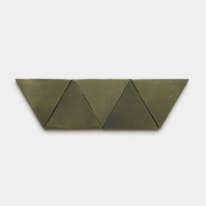 Four Oyamel Triangle tiles by Zia Tile, in a greenish-gray hue, are arranged in a row with two triangles at the center and two trapezoids at each end, set against a plain white background.