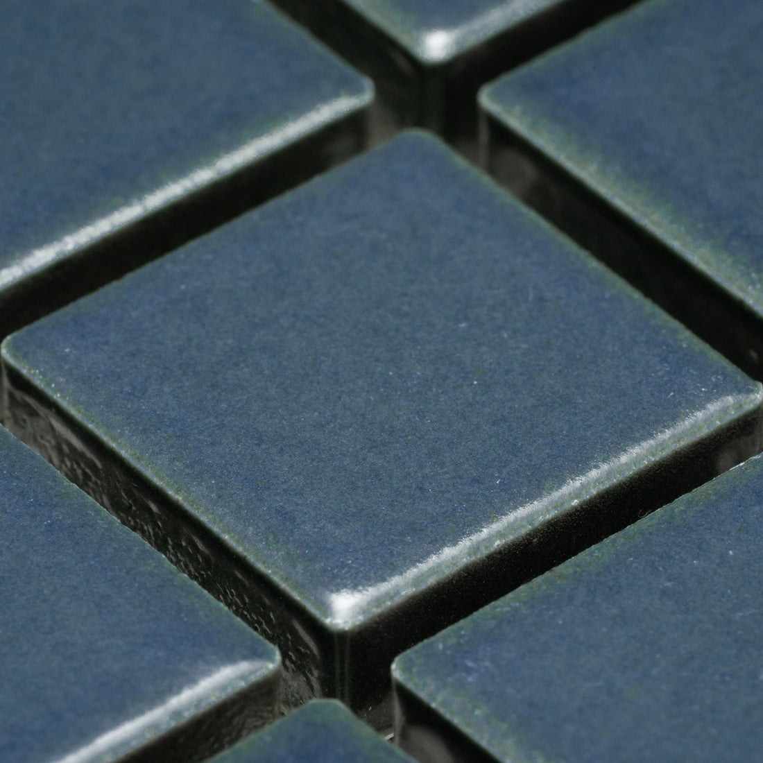 Close-up of Zia Tile's Pacific Blue 1x1 ceramic tiles, featuring a subtle texture and deep blue hue, arranged in a grid pattern with visible grout lines.