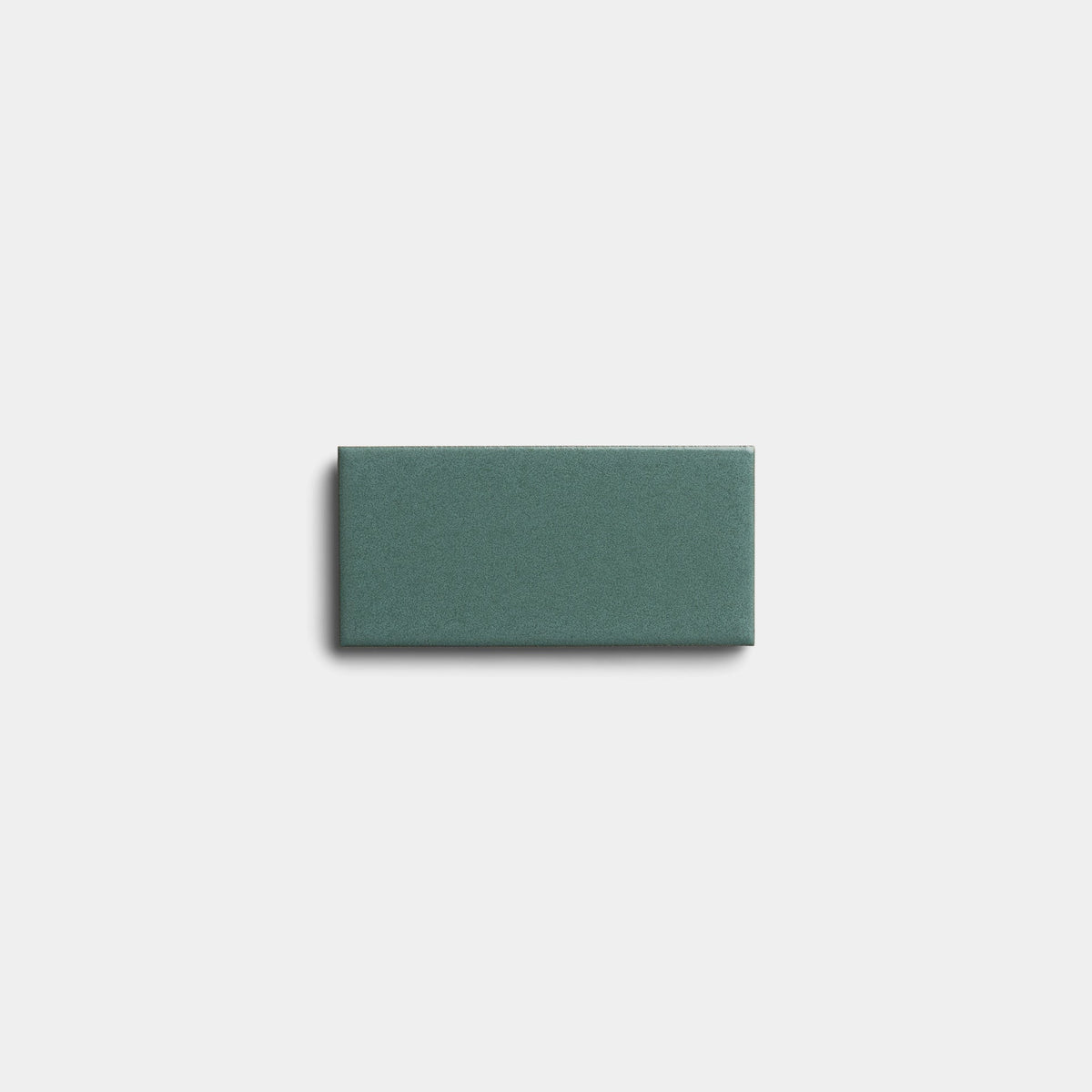 A single Patina 2x4 sample tile by Zia Tile in teal ceramic rests on a plain white background, casting a soft shadow to the left and below.