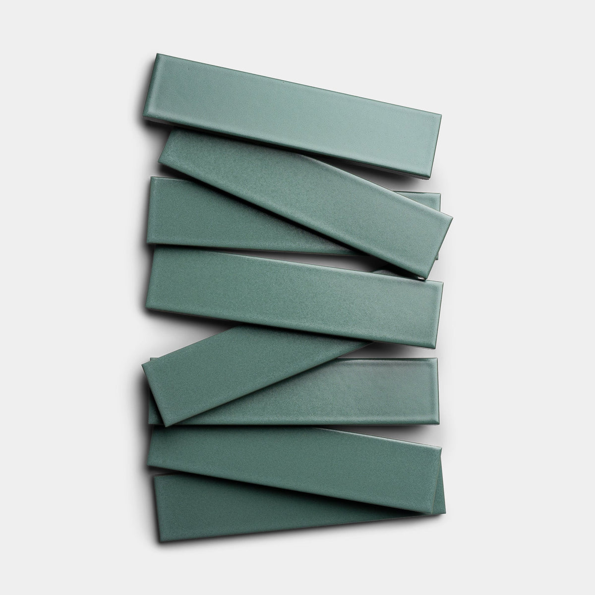Seven rectangular Patina 2x8 tiles by Zia Tile in teal are stacked in a slightly staggered, overlapping arrangement against a white background.