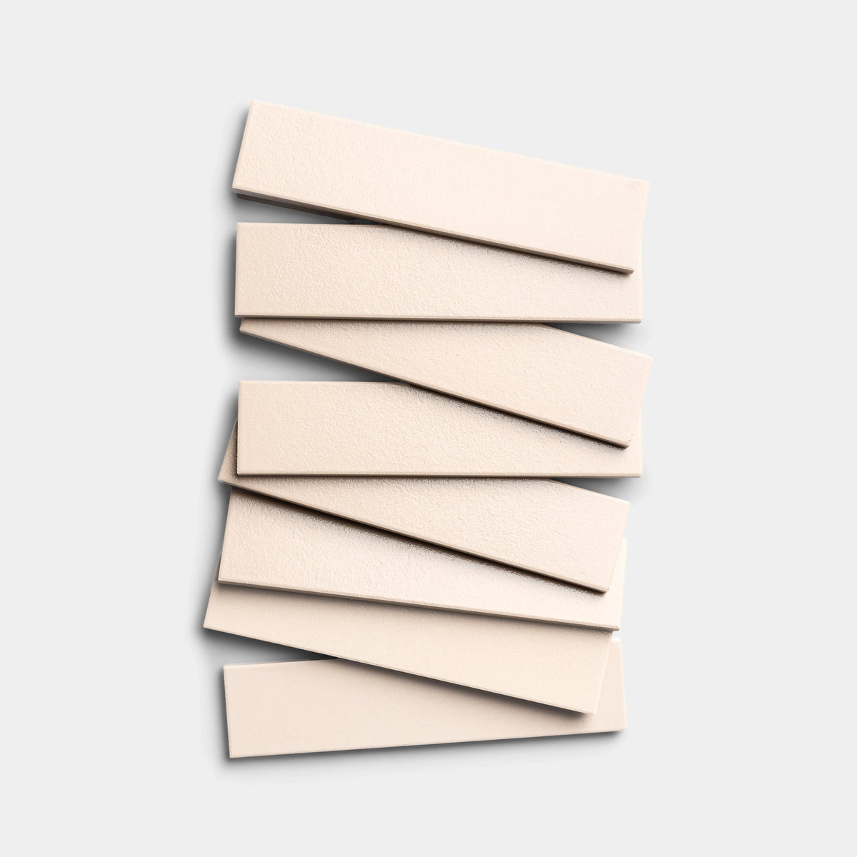 Seven rectangular Peach Blossom 2x8 tiles by Zia Tile are stacked in a slightly offset, vertical arrangement on a plain, light gray background.