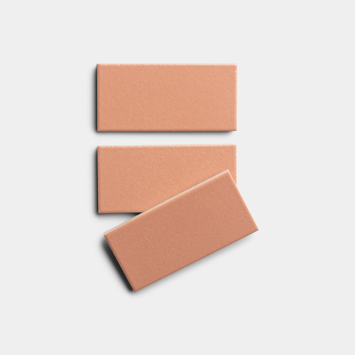 Three rectangular, matte Pecan 2x4 tiles by Zia Tile are arranged on a light gray background: two stand vertically, while the third is slightly tilted at the bottom.