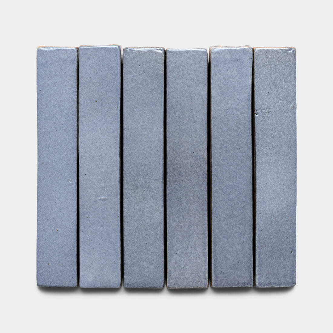 Six Pedregal Mini Bar tiles by Zia Tile are arranged side by side against a white background, featuring a smooth, matte blue-gray finish with subtle variations in color and texture.