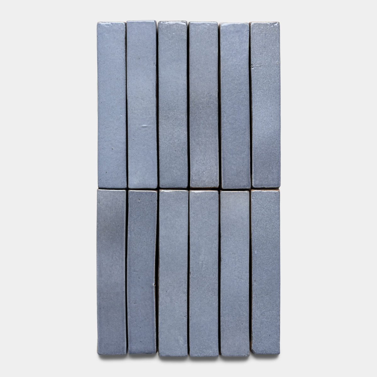 Twelve Pedregal Mini Bar tiles by Zia Tile, rectangular and blue-gray, are arranged vertically side by side in two rows of six against a plain white background.