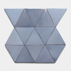 Twelve blue Pedregal Triangle tiles by Zia Tile are arranged in a geometric pattern—two rows of four triangles between two rows of two inverted triangles—set against a light grey background.